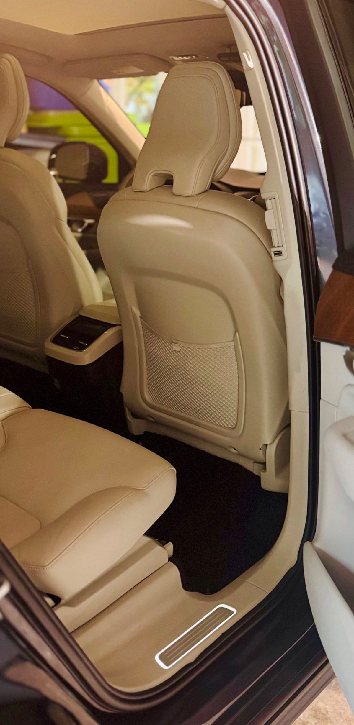Interior view of a beige leather car seat with a headrest, visible through an open door.
