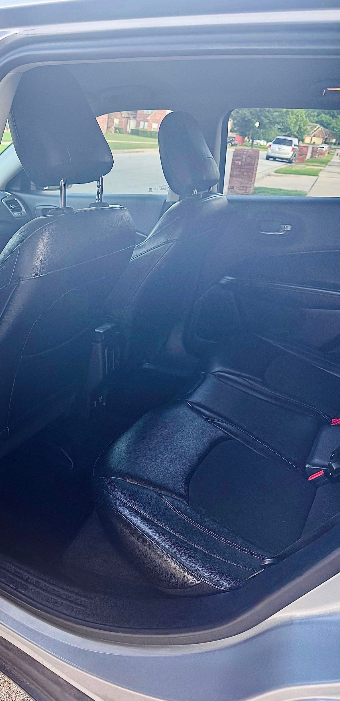 Interior view of the backseat of a car with black leather seats and headrests, showing a view of the outside.