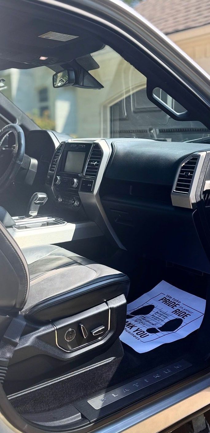 Interior view of a gray Ford truck, showing the dashboard, driver's seat, and a floor mat with writing.