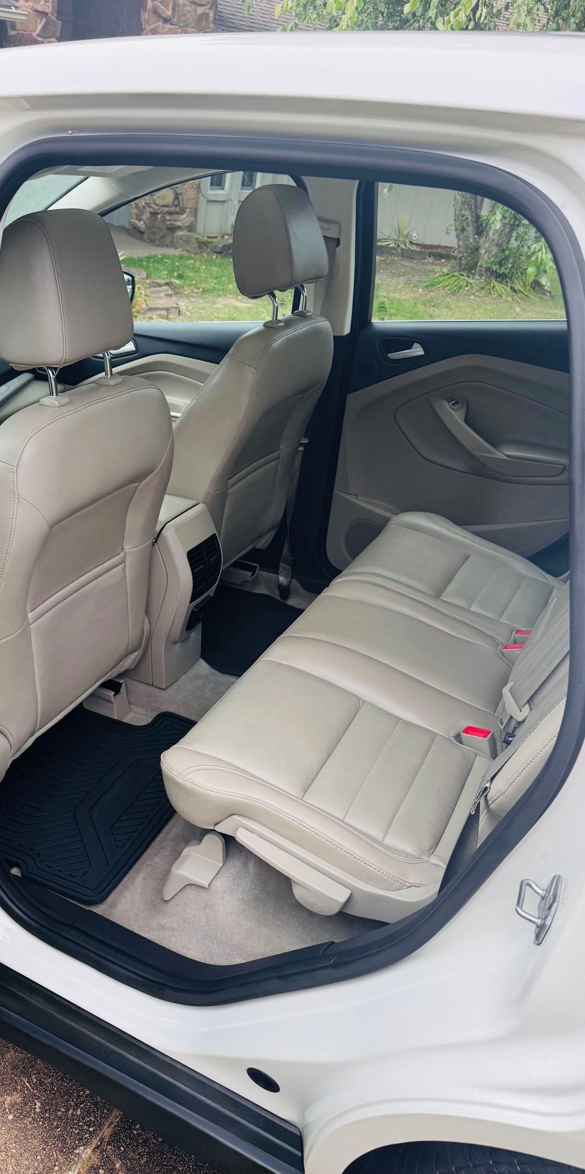 Interior view of a beige car. The back seats are folded up, revealing the floor. The setting appears to be outdoors.