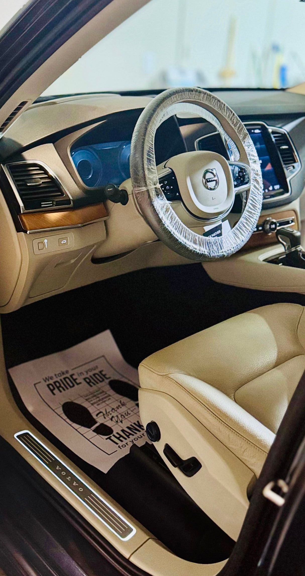 Interior of a Volvo car with tan leather seats, steering wheel cover, and floor mat.