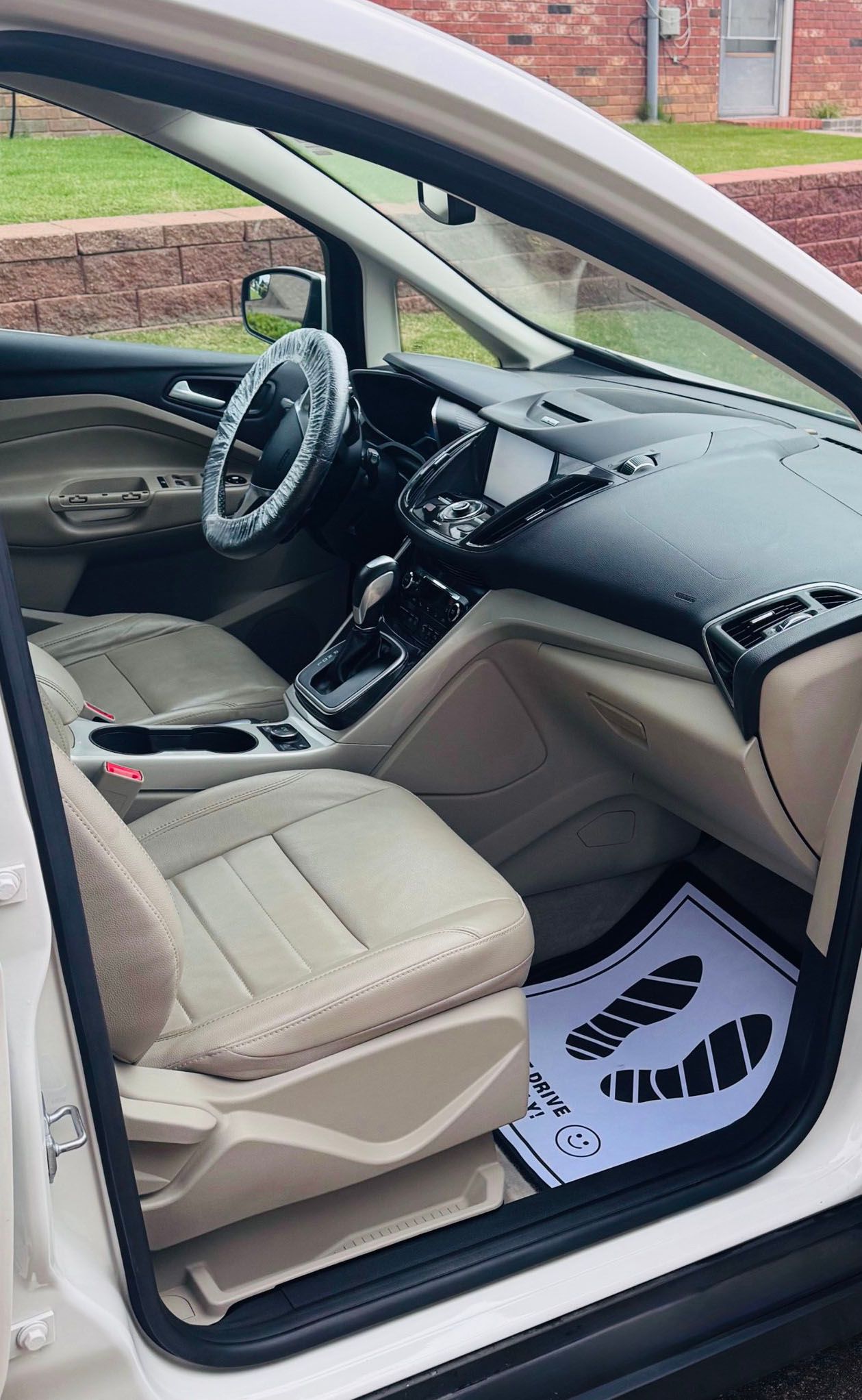 White car interior with tan seats, steering wheel cover, and floor mat with footprint graphic.