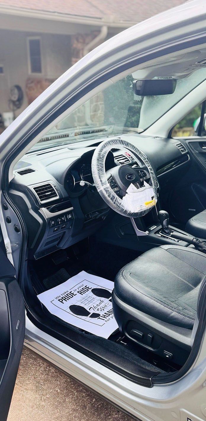 Interior of a silver car. Driver's seat, steering wheel covered, floor mat, dashboard visible.