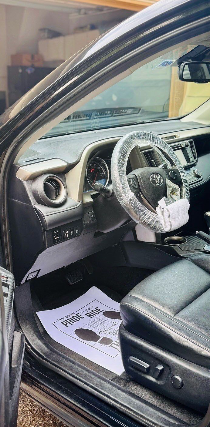 Interior of a black Toyota RAV4.  The steering wheel has plastic wrap. A foot covering paper is on the floor.