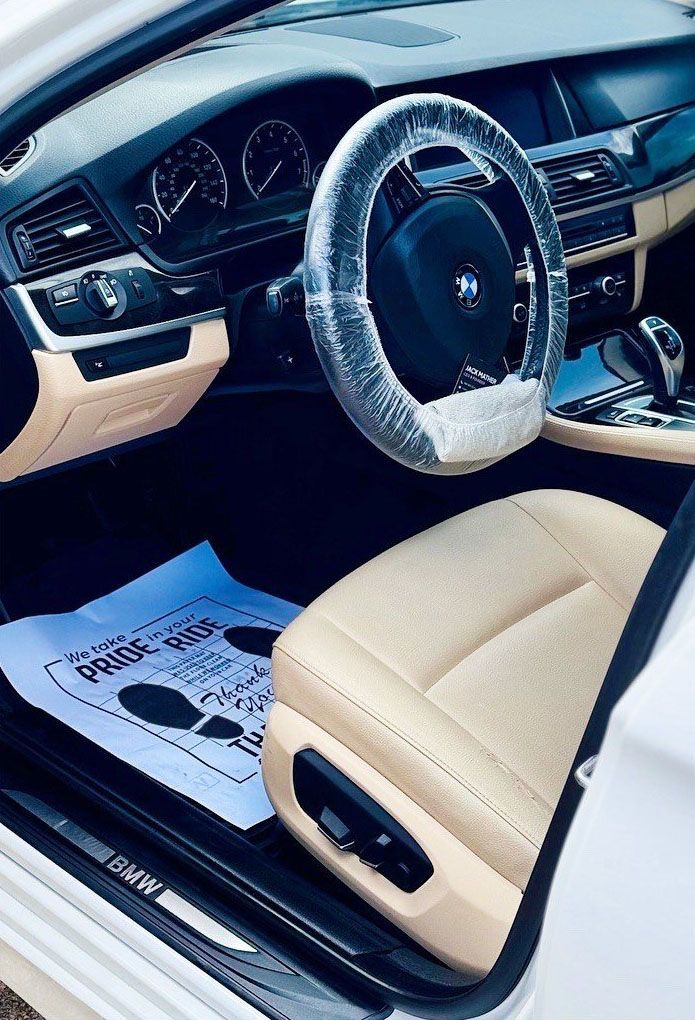 Interior view of a white BMW car with tan leather seats and a plastic-wrapped steering wheel.