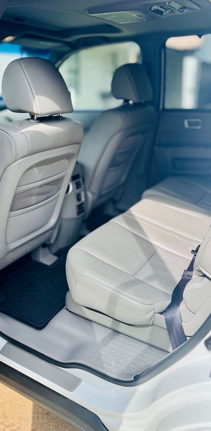 Interior view of the backseat of a white SUV with light gray seats, a seat folded up, and a dark floor mat.