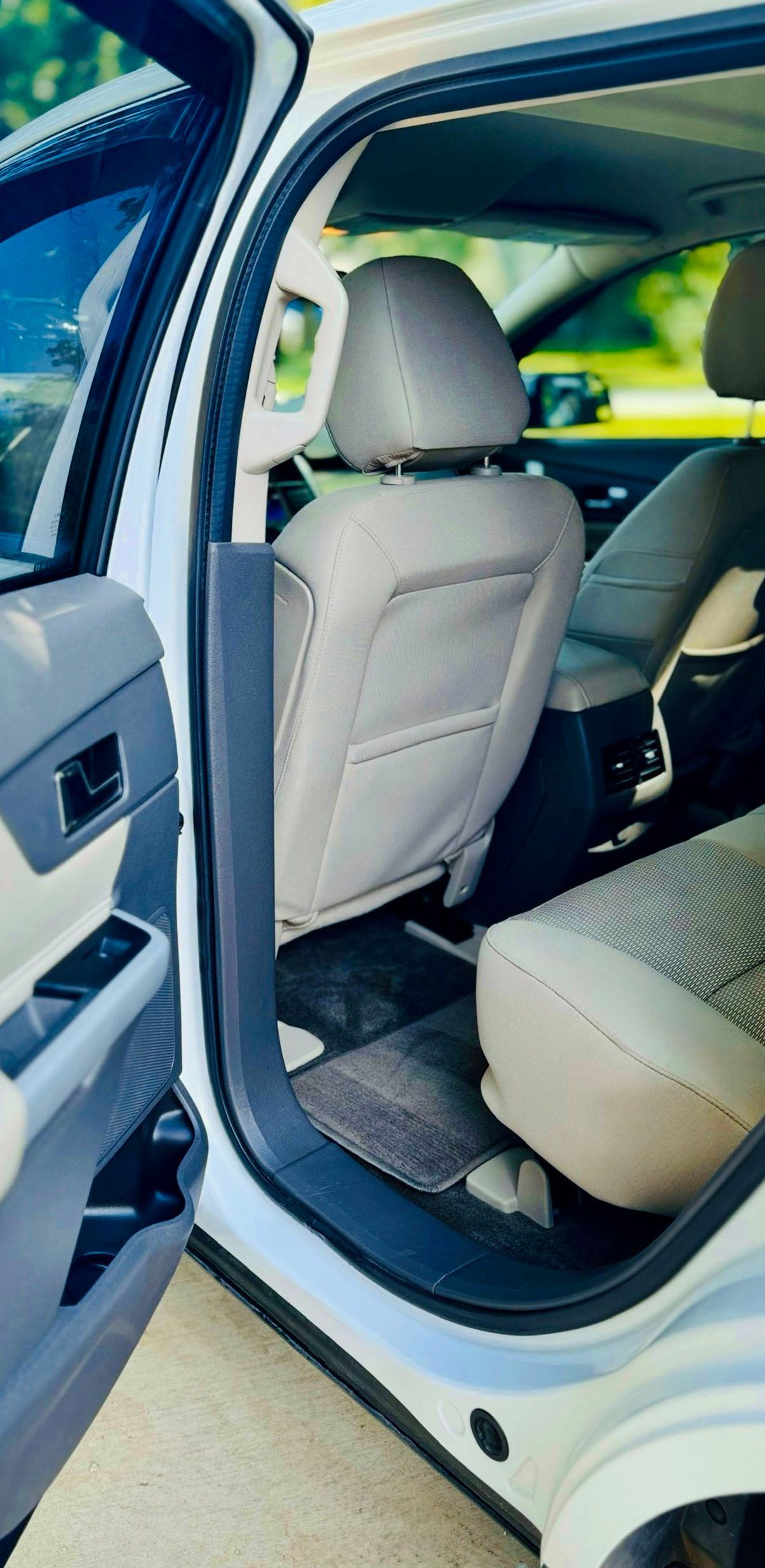 Interior view of a white SUV's back seat with beige fabric seats and a black floor mat.
