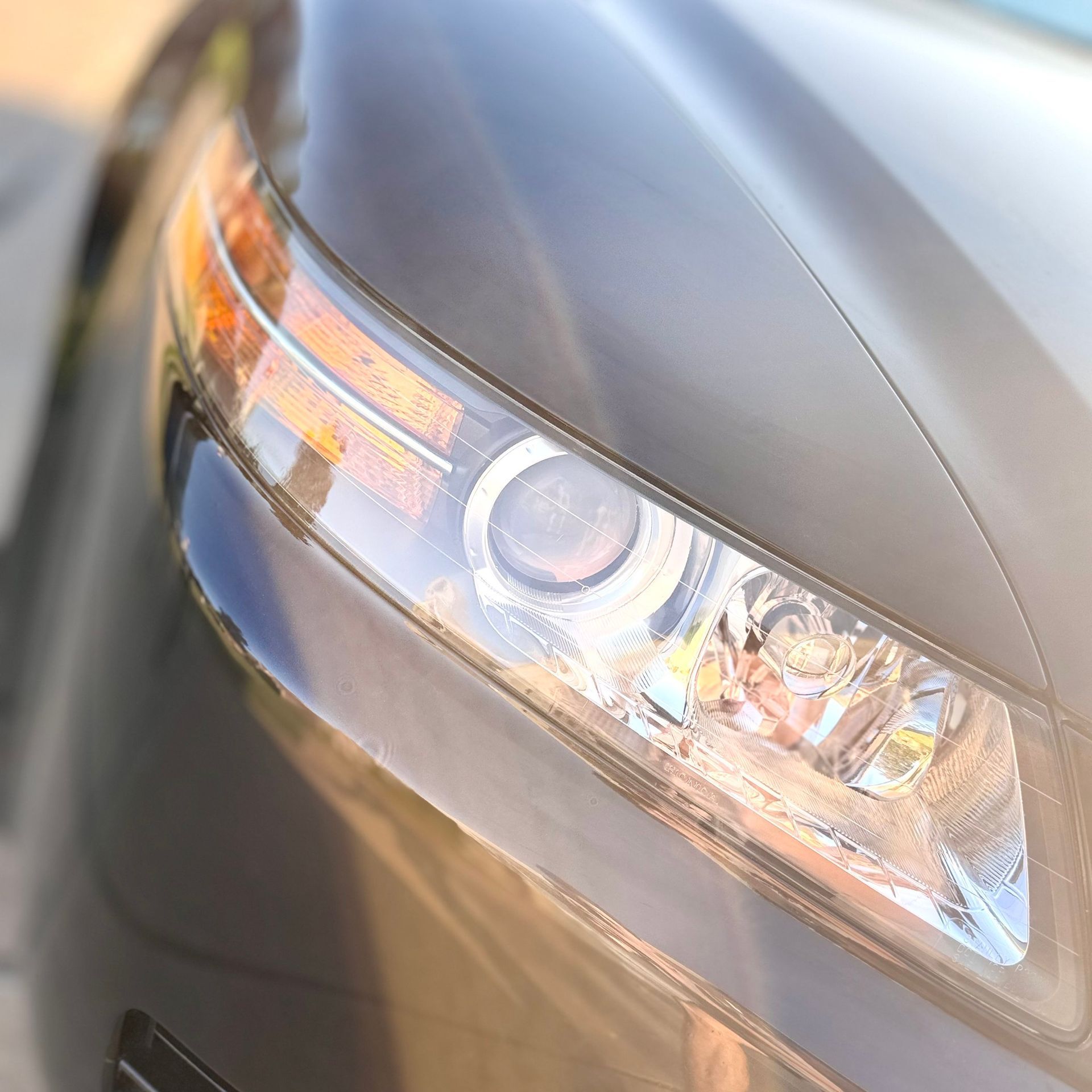 Close-up of a gray car headlight with orange turn signal; sunlight reflects off the glass.