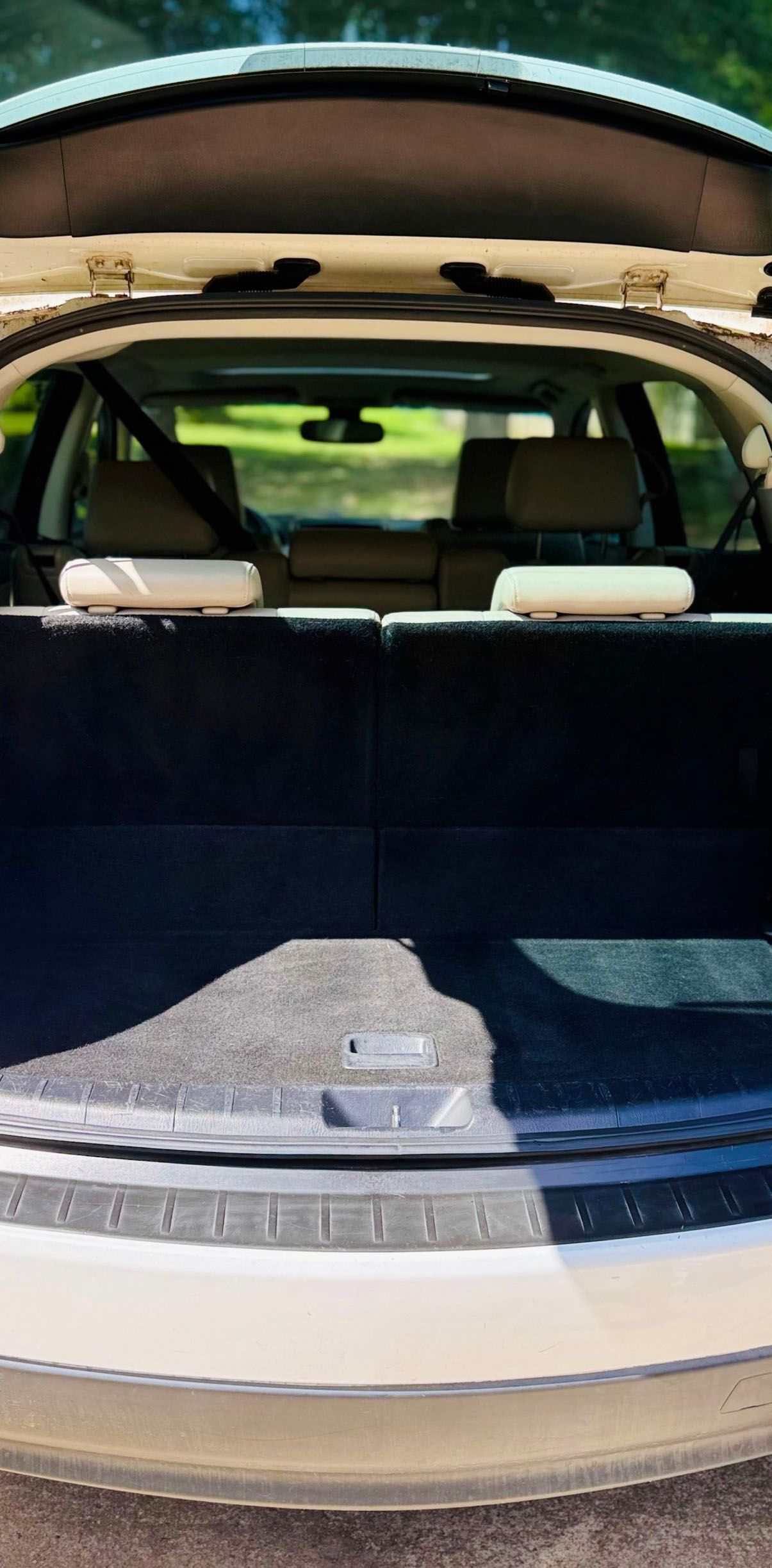 The open trunk of a light-colored car.  The rear seats are visible, along with the interior. Outdoors.