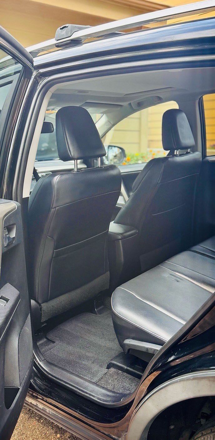 Black interior of a vehicle with dark leather seats, and the rear door open.