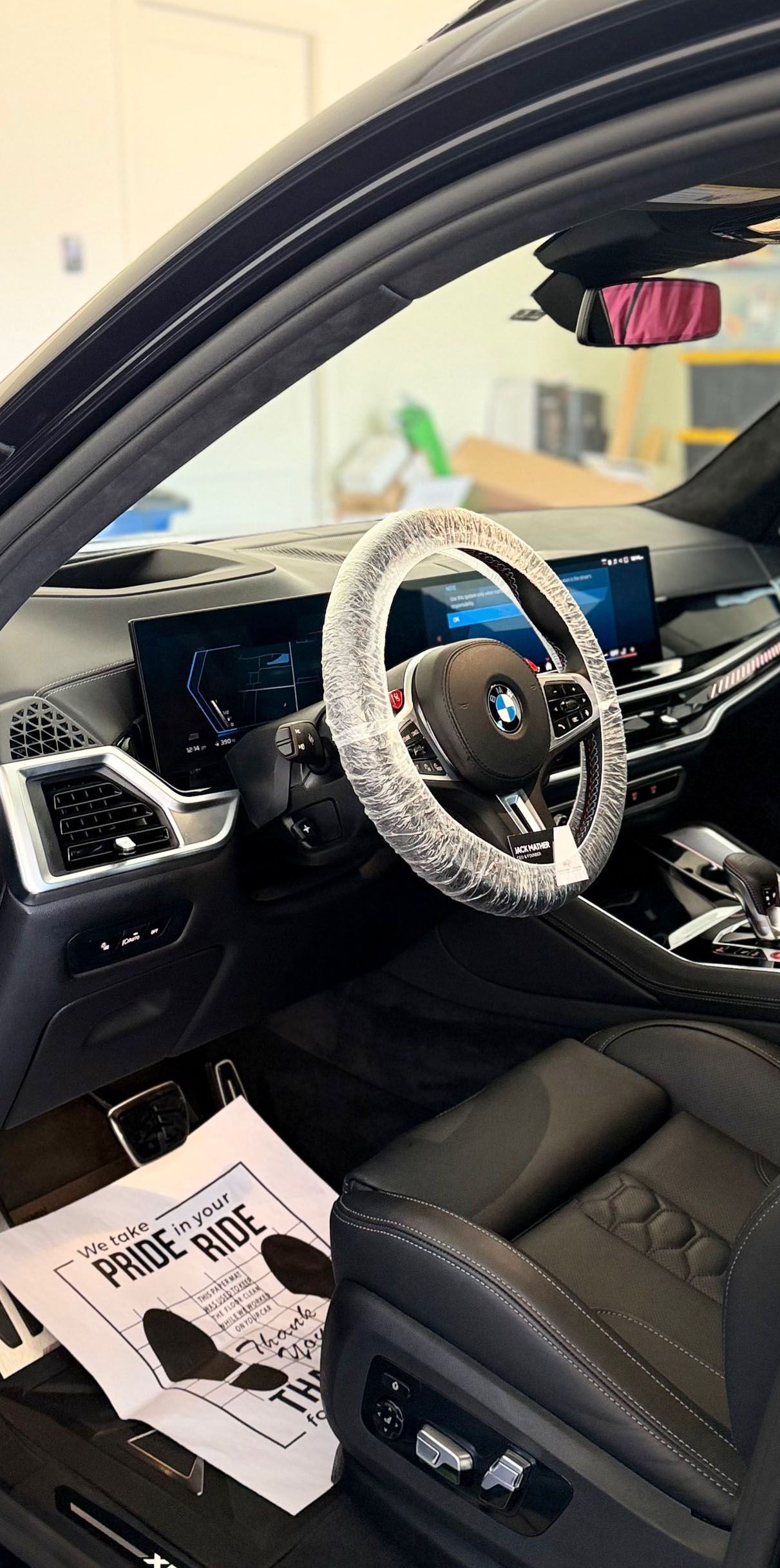 Interior of a black BMW, steering wheel and seats covered in plastic. Paper on floor.