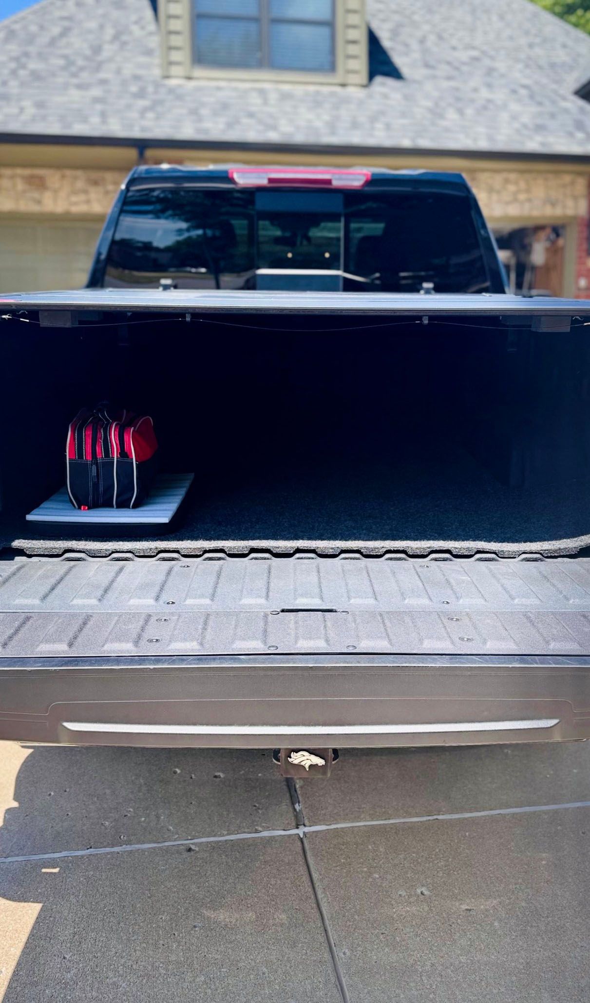 Open truck bed with red items on a white surface, driveway visible, house in the background.