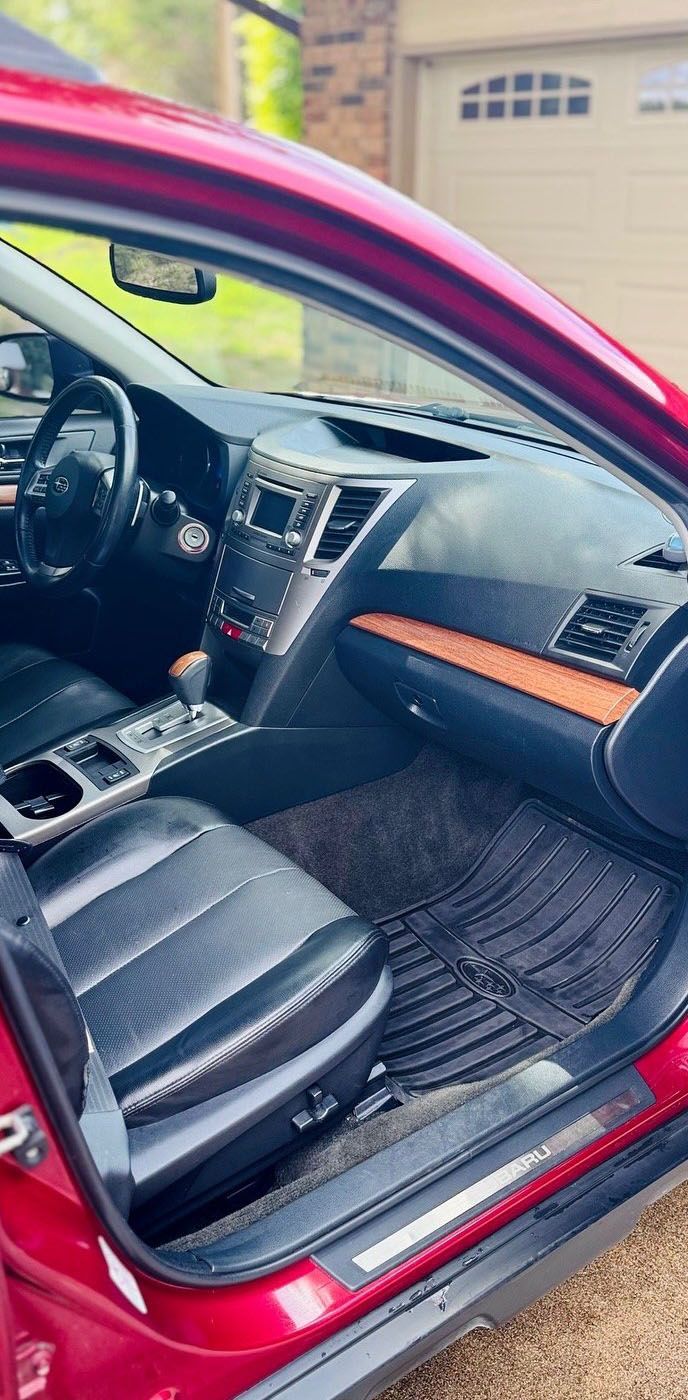 Interior of a red Subaru, with black leather seats, dashboard, and a brown wood trim.
