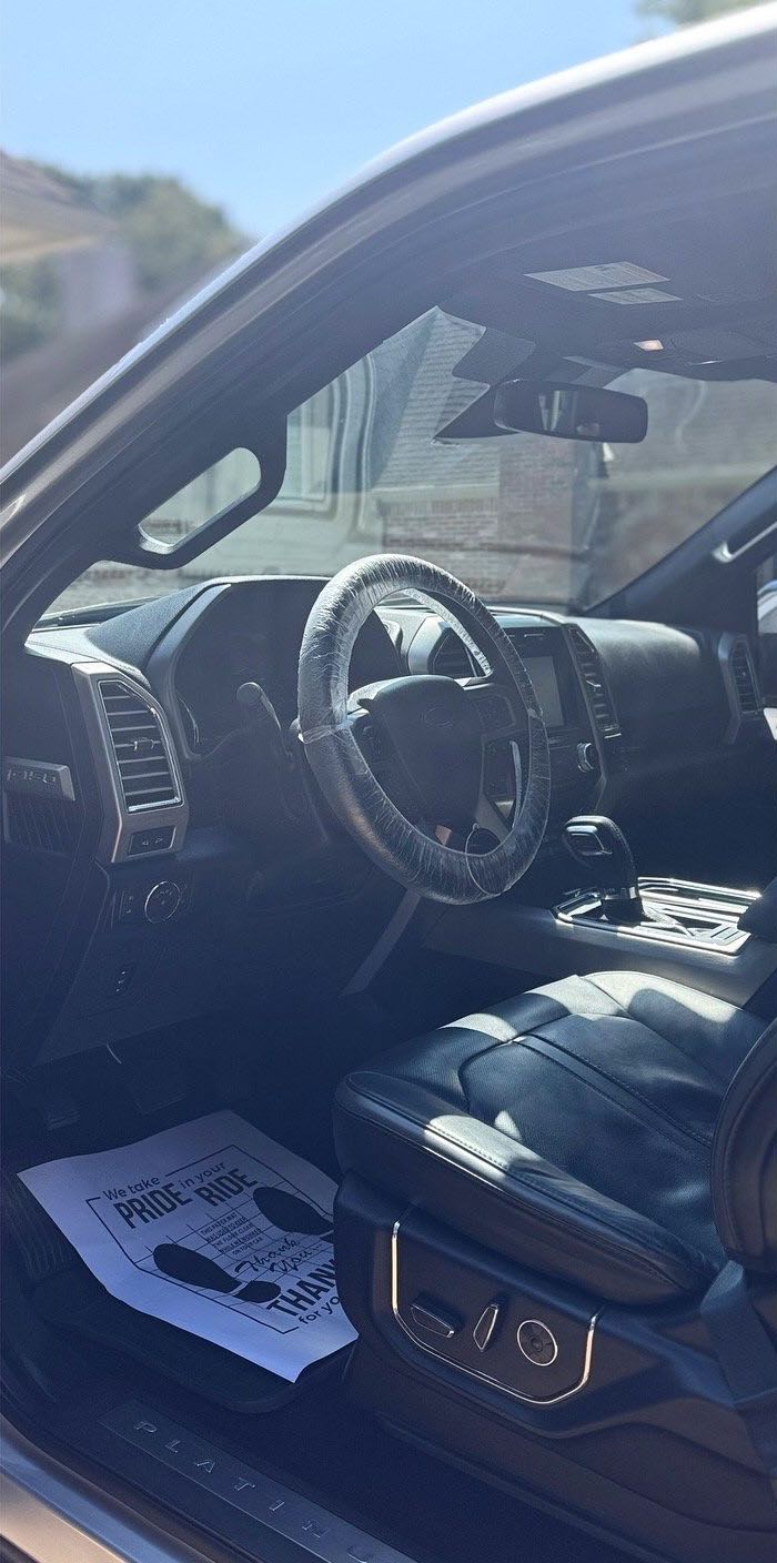 Interior of a black vehicle, showing the dashboard, steering wheel, and front seat. A paper is on the floor.