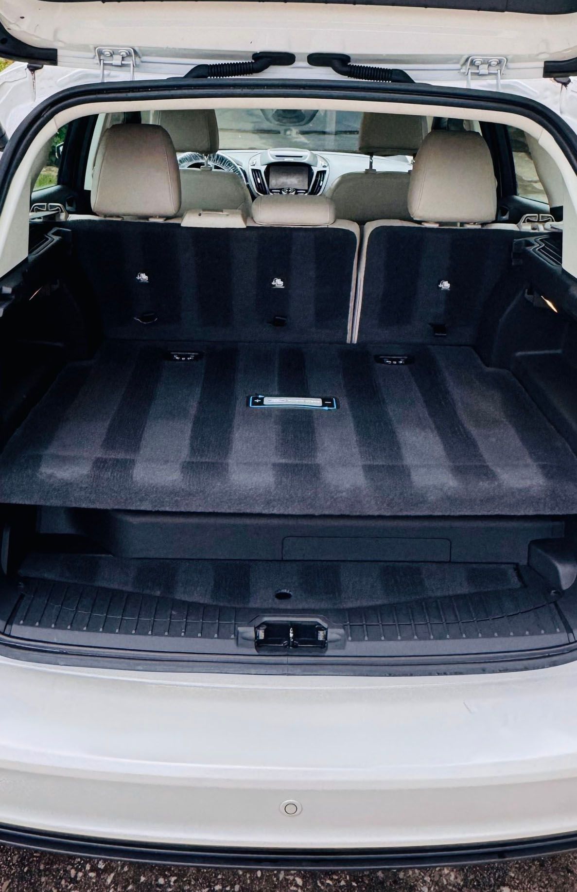 Open white car trunk with clean, dark gray carpet and rear seats visible.