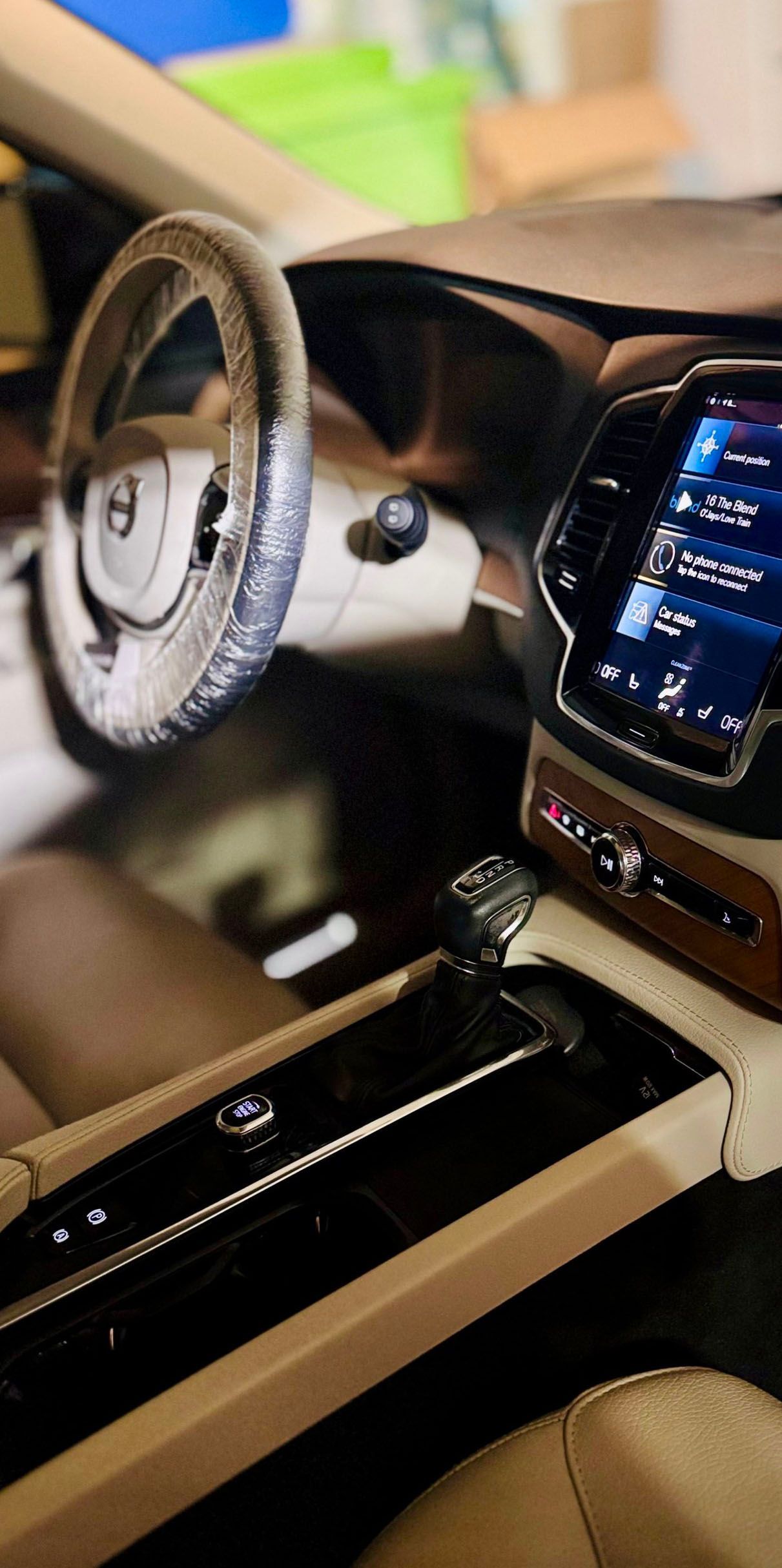 Interior of a beige and black Volvo SUV, including the dashboard, steering wheel, and gear shift.