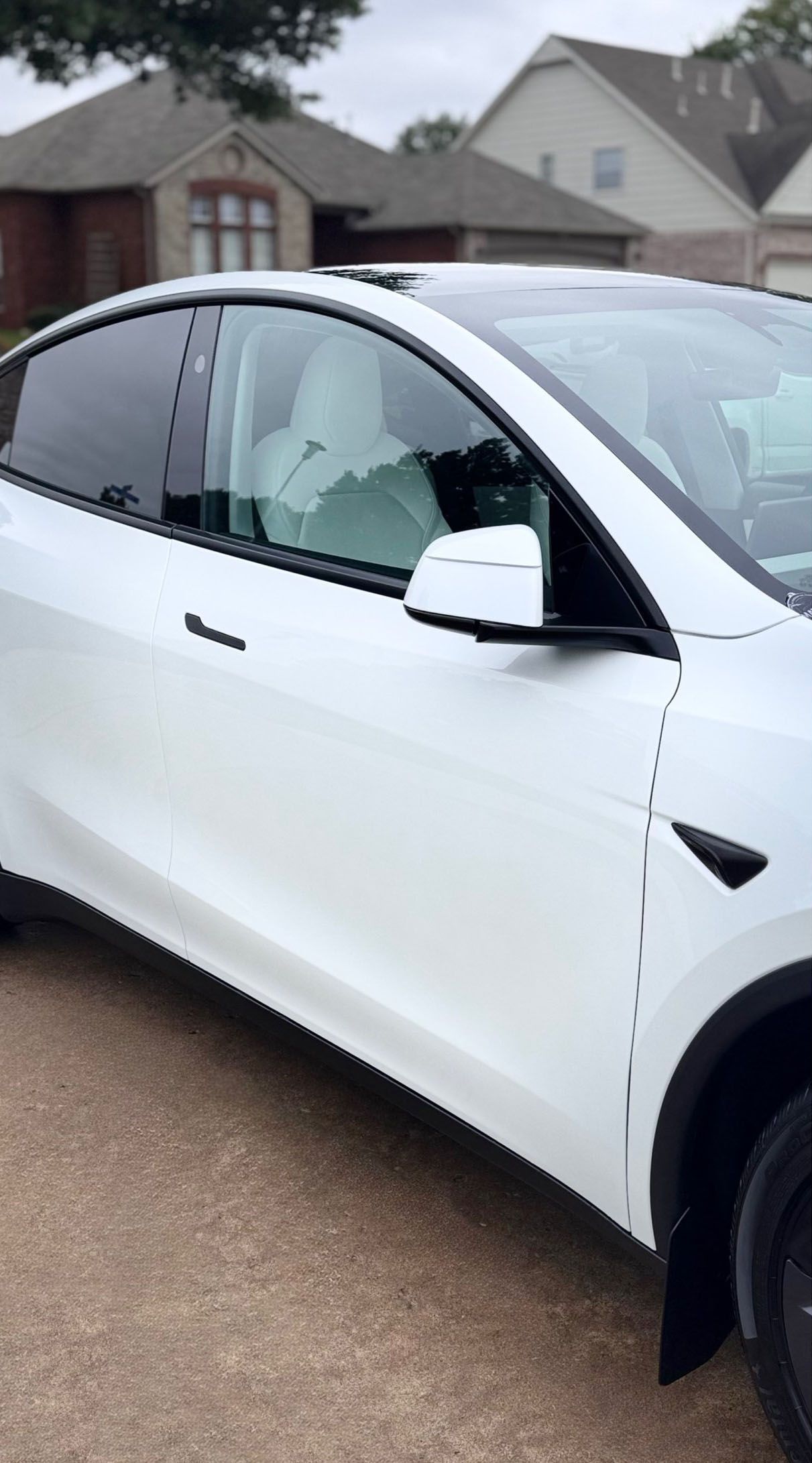 White Tesla Model Y parked on a street in front of houses; cloudy day.