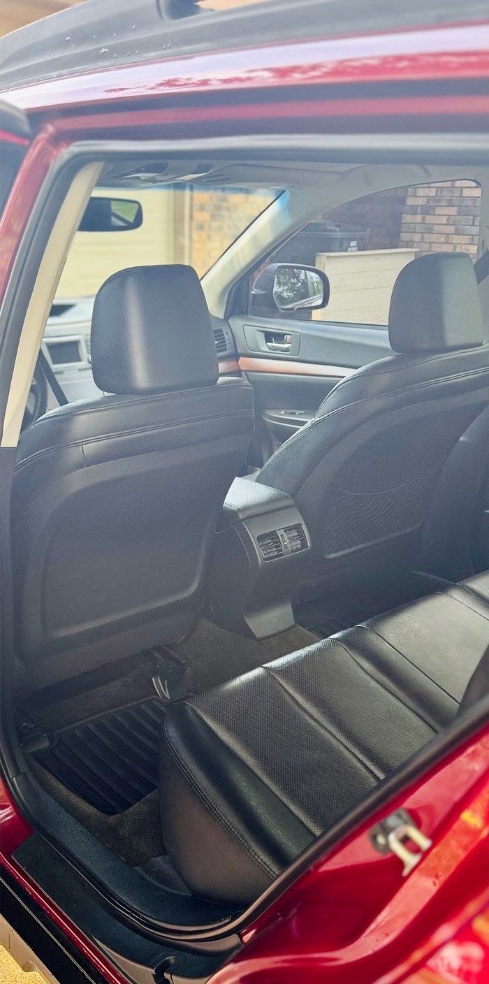 Interior view of a red car with black leather seats. Rear seats visible with center console and floor mats.
