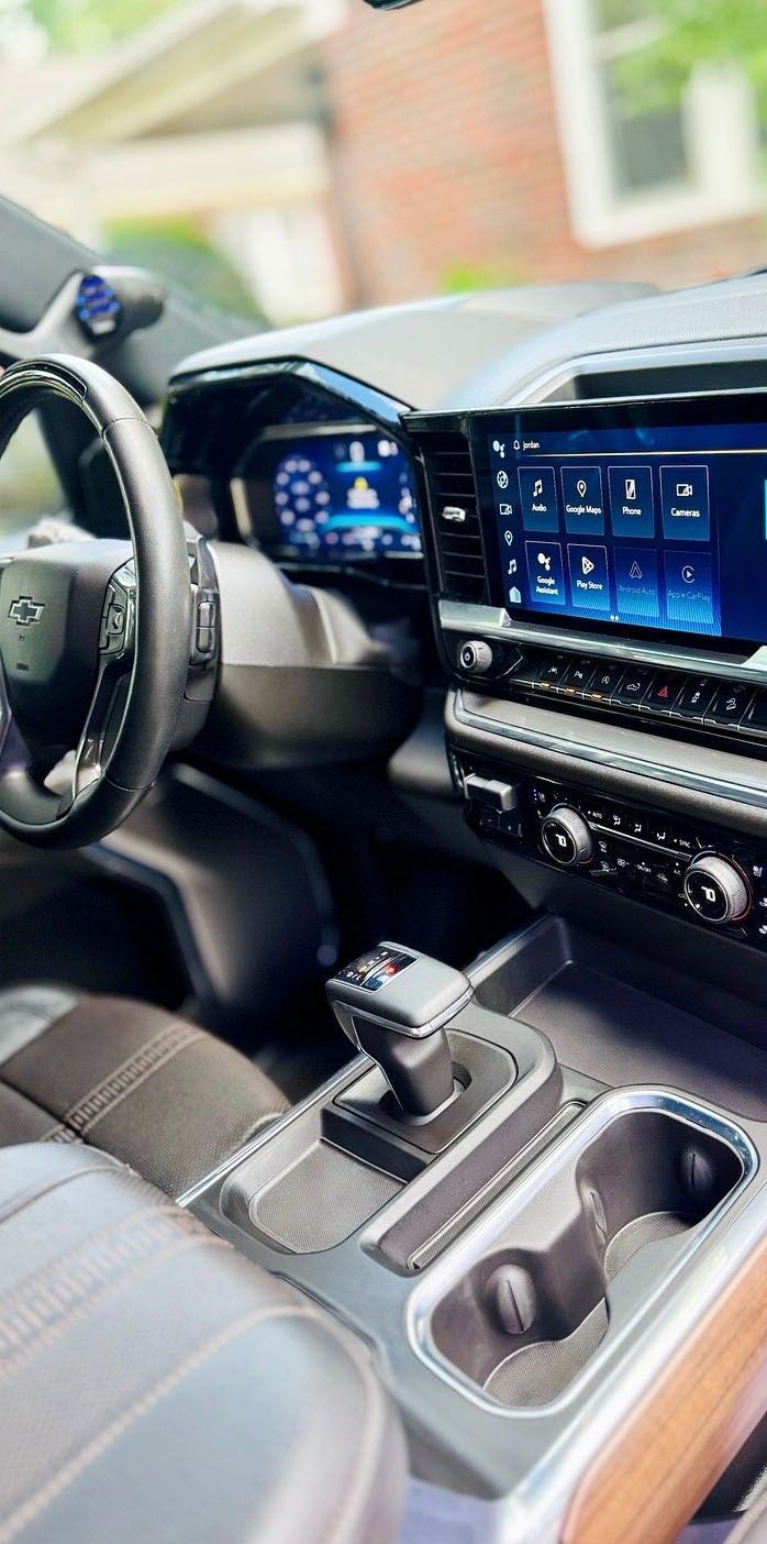 Interior view of a modern car's dashboard with large screens, gearshift, and cup holders.