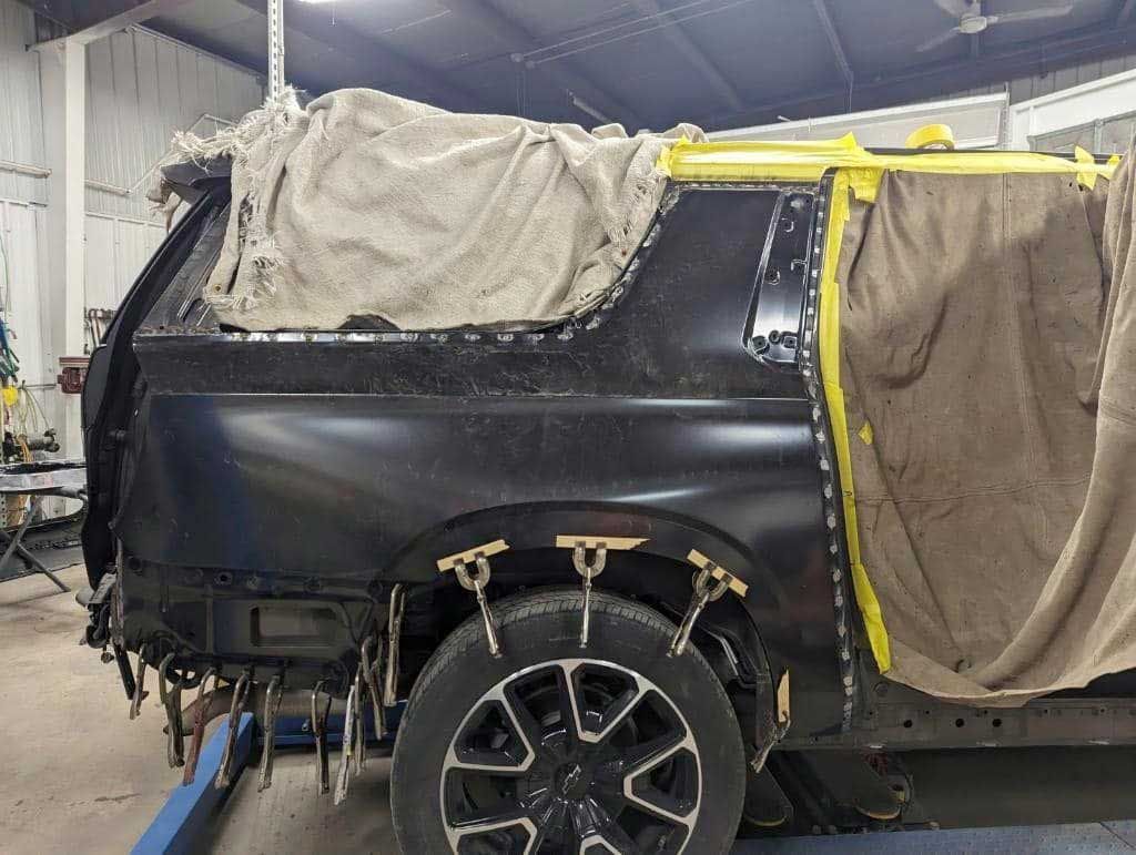Black car body with repair clamps in an auto body shop.