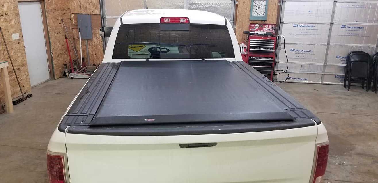 A white pickup truck with a black bed cover inside a garage.