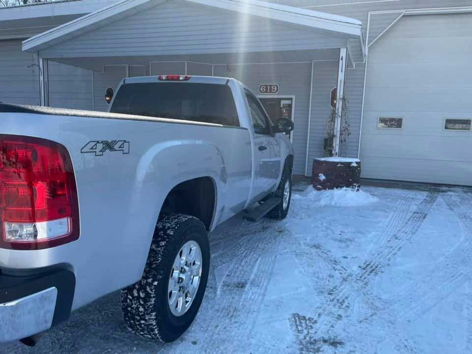 Silver pickup truck parked outside a building with a garage door in a snowy setting.