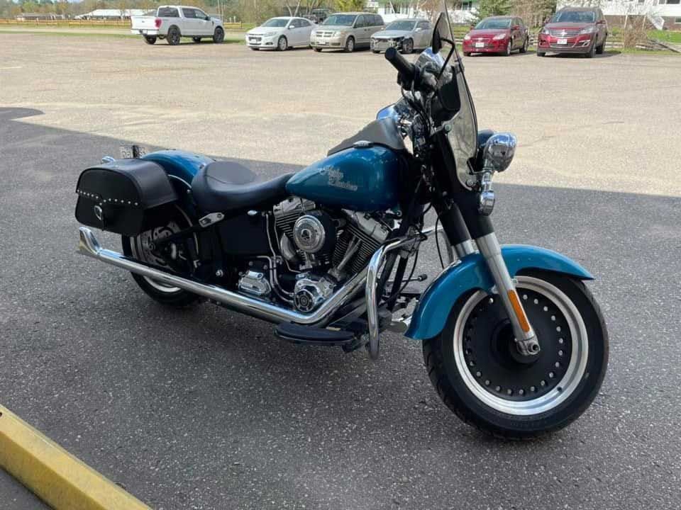 Teal Harley-Davidson motorcycle parked on asphalt. Features include saddlebags and a windshield.