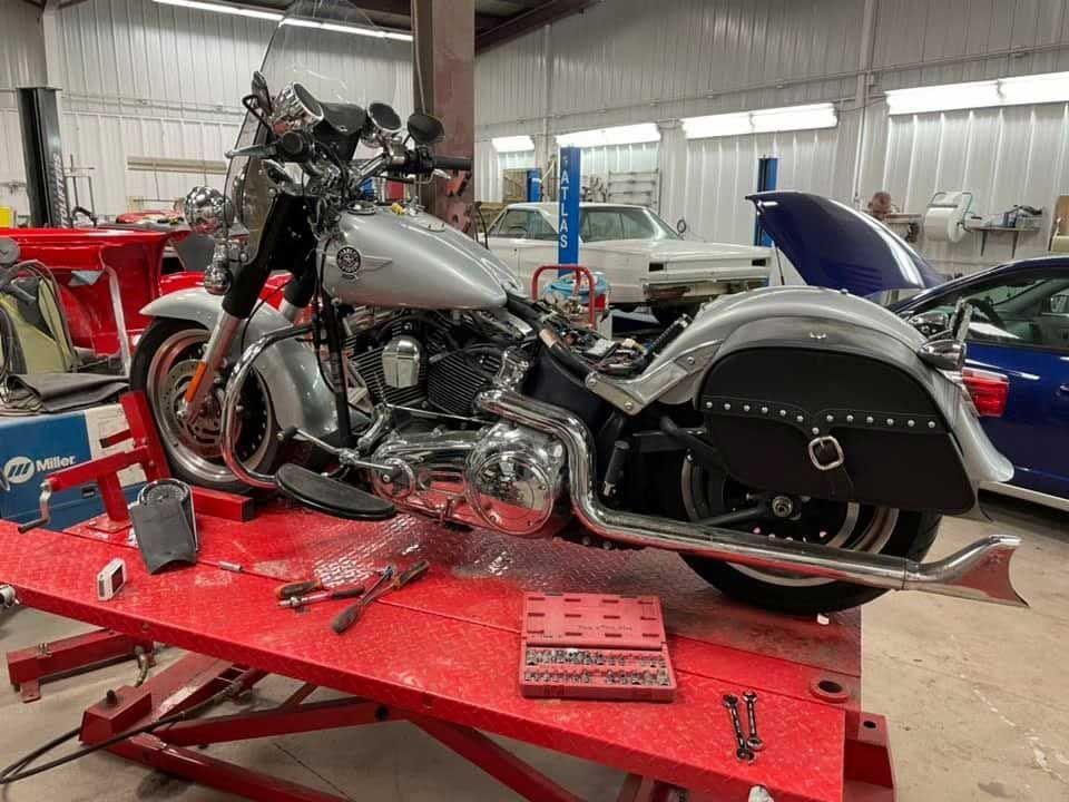 Silver Harley Davidson motorcycle on a red lift in a garage; tools and other vehicles visible.