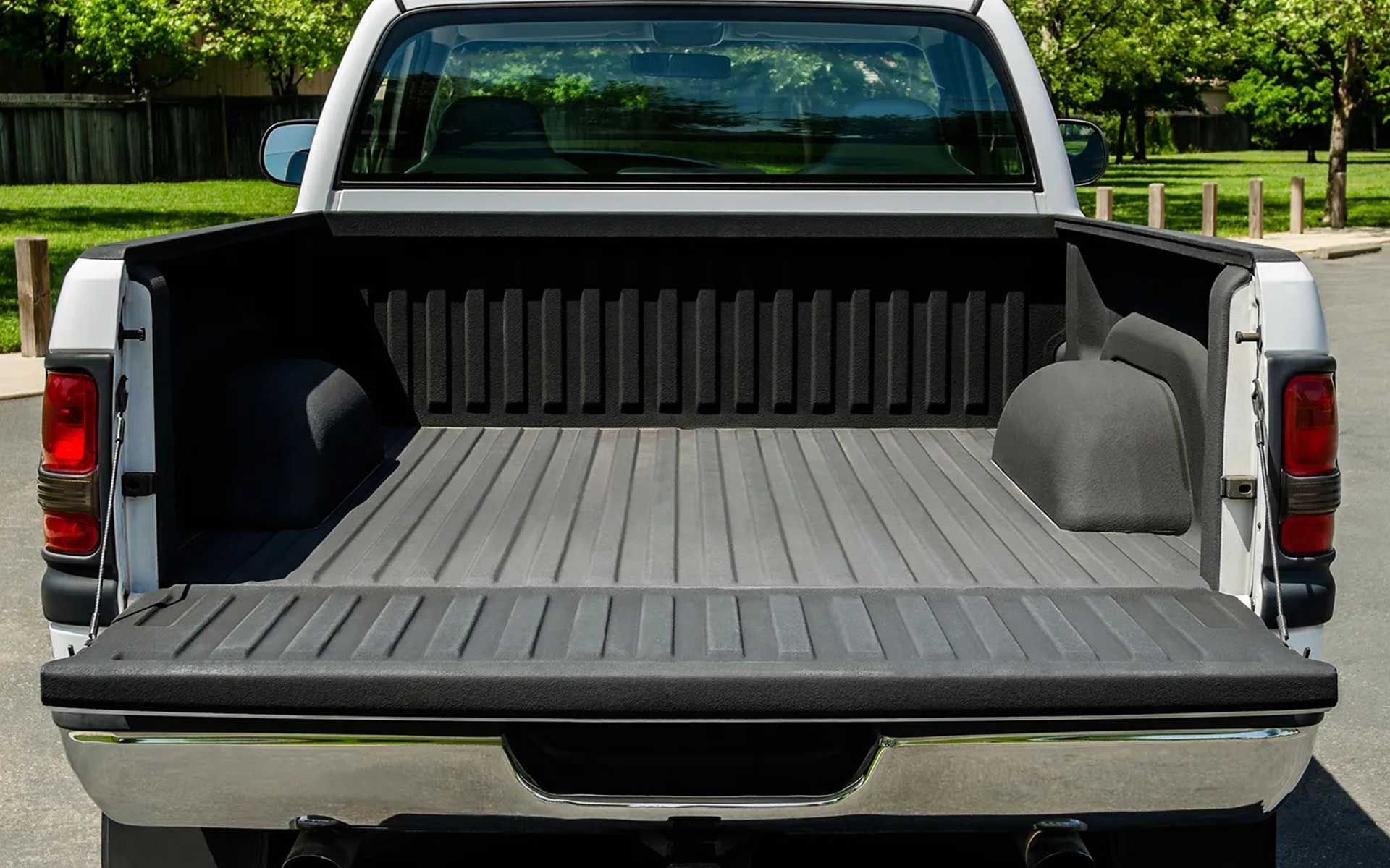 Rear view of a white pickup truck bed, with a black bed liner and tail lights; outdoors.