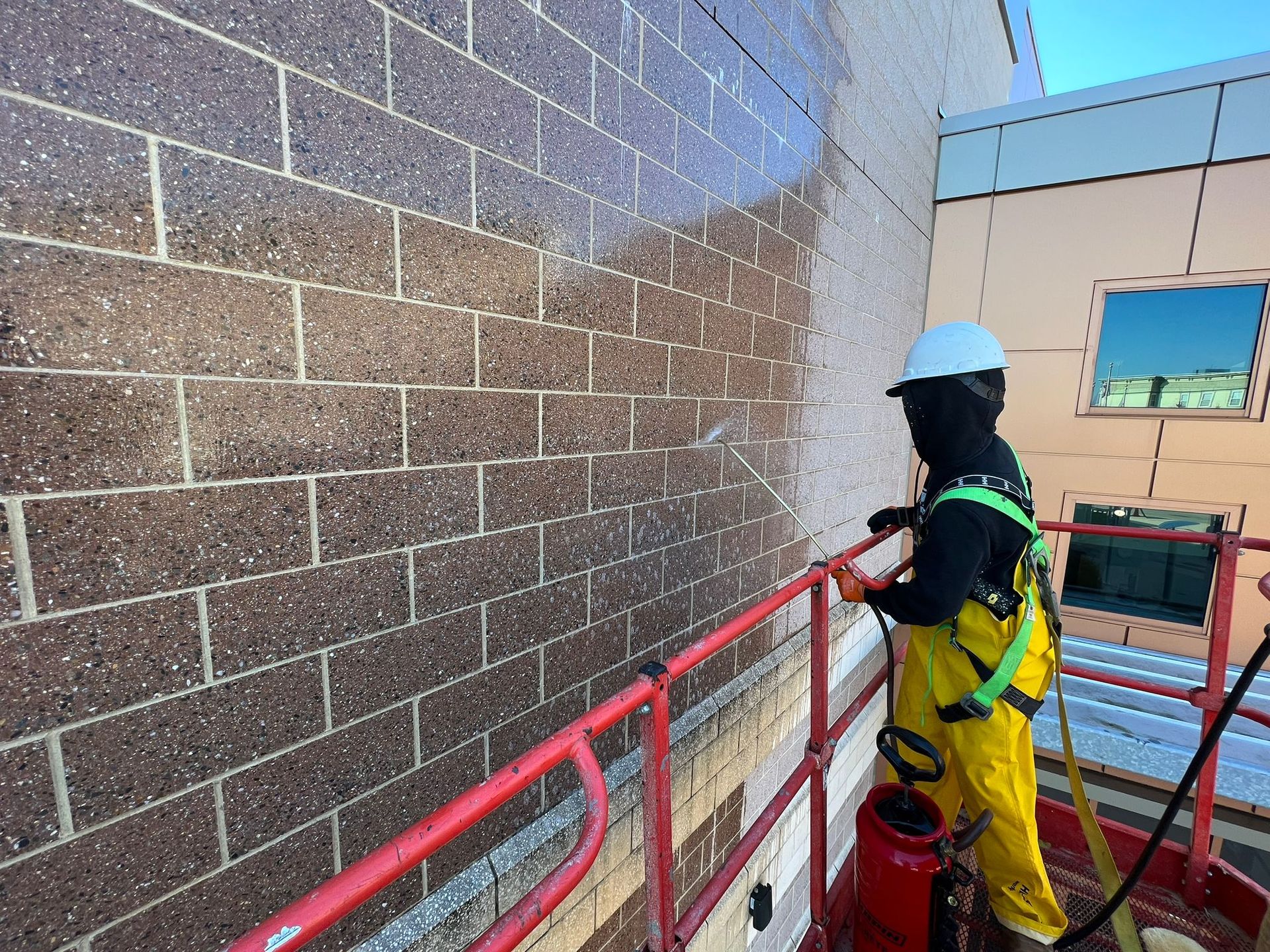 A man in yellow PPE is cleaning a brick wall