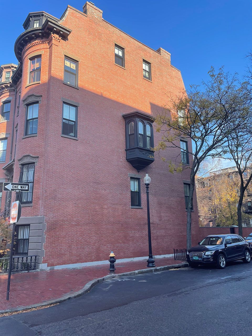 Brick building on a street corner with a bay window and dark car parked nearby.