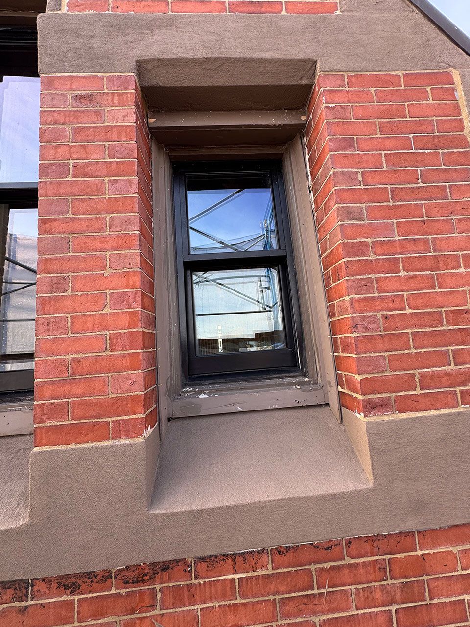 Brick building exterior with a black-framed window set in a recessed area with brown trim.