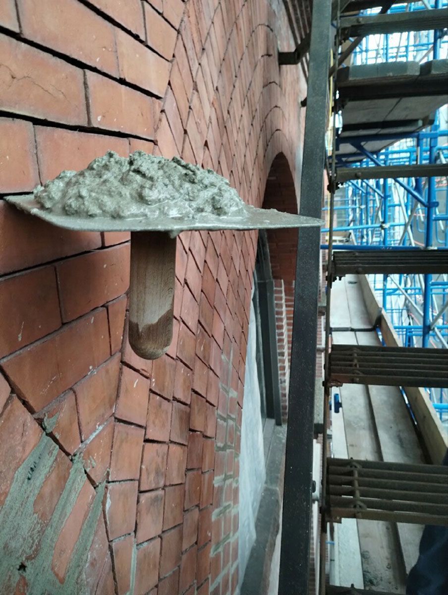 A trowel filled with concrete is hanging on a brick wall