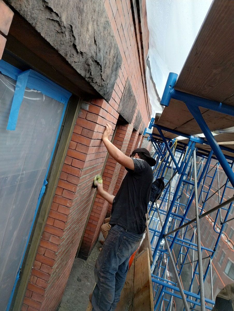 A man is standing on a scaffolding cleaning a brick wall