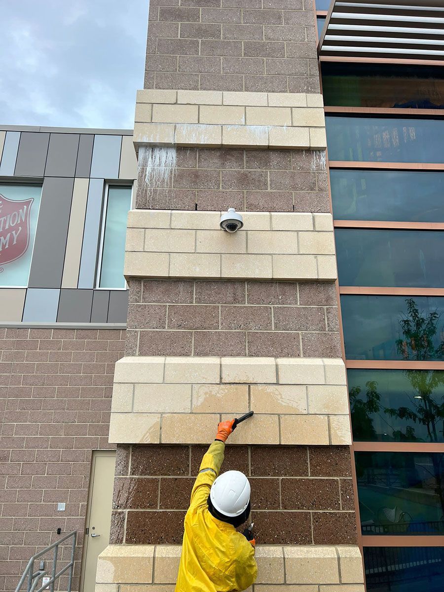 A man in yellow PPE is cleaning a brick wall