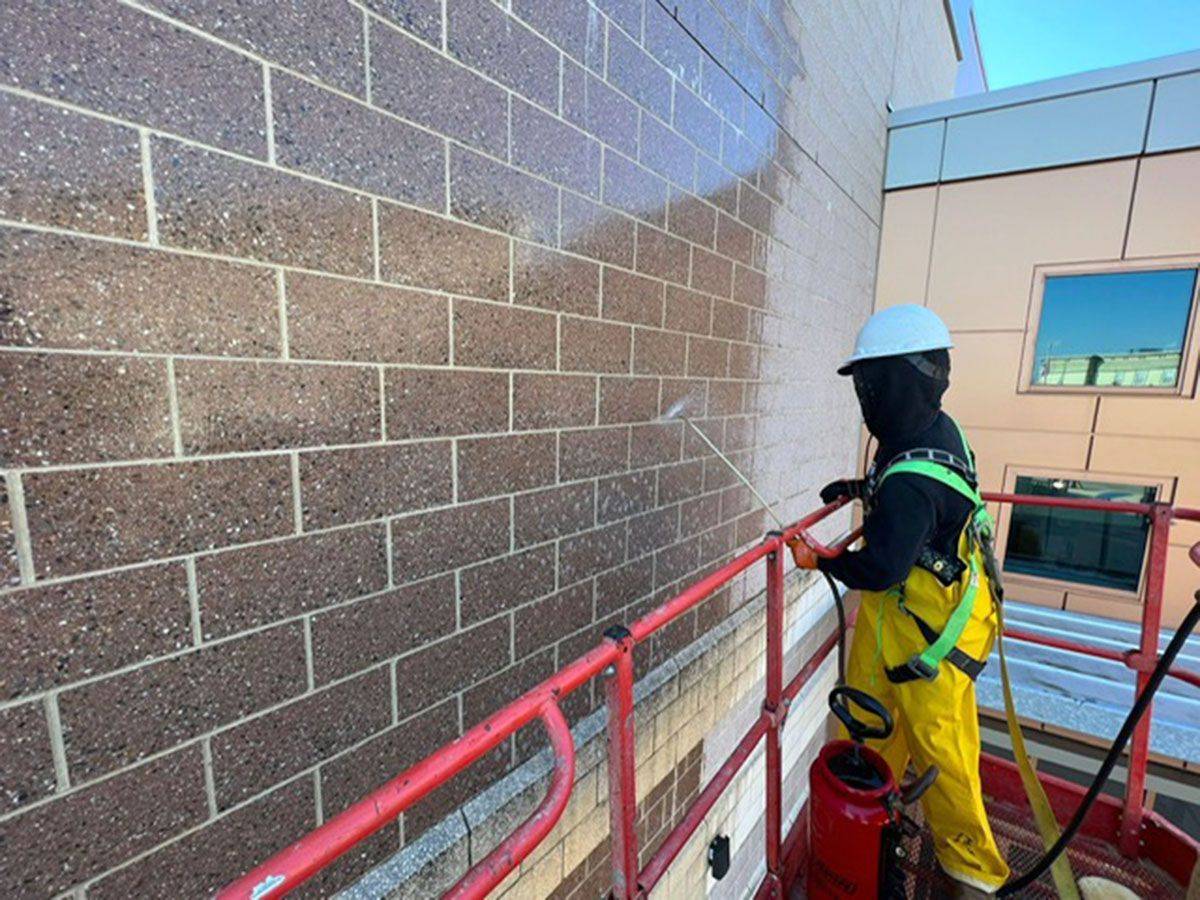 A man is spraying a brick wall with a high-pressure washer