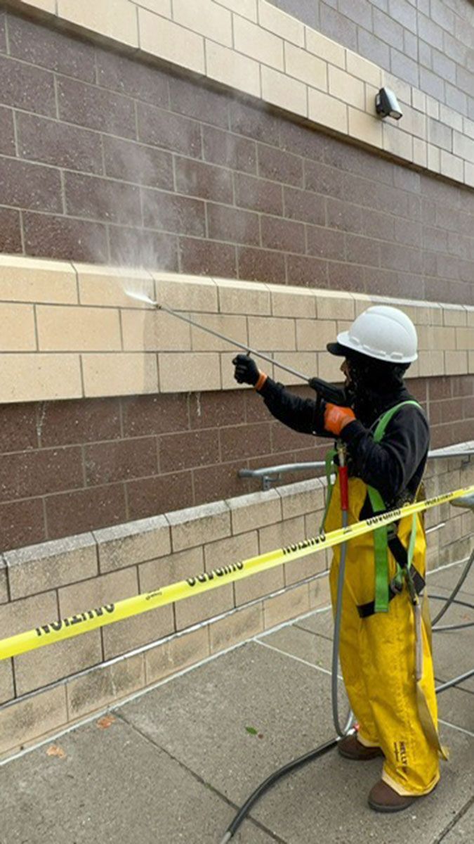 A man in PPE is spraying a brick wall with a high-pressure washer