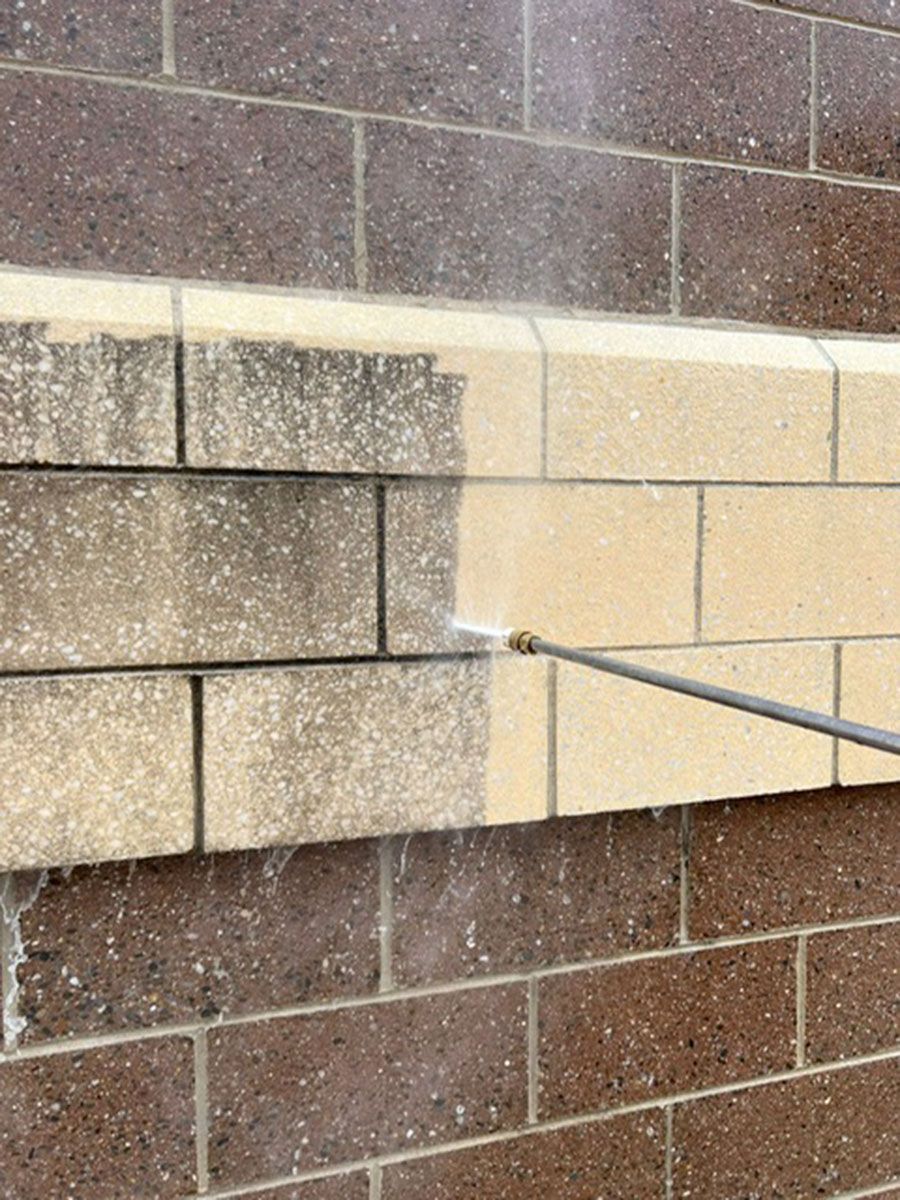 A brick wall with stain is being cleaned with a high-pressure washer