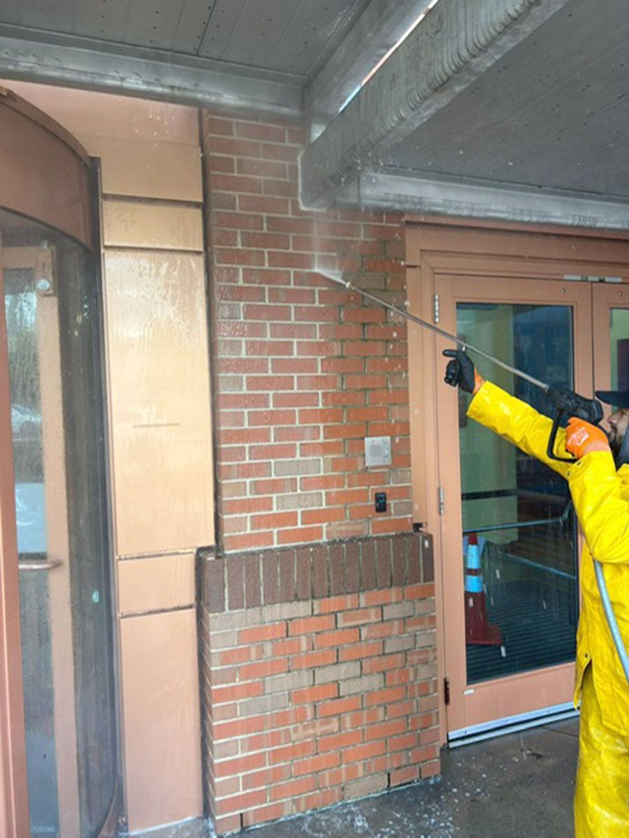 A man in yellow PPE is cleaning a brick wall with a high-pressure washer
