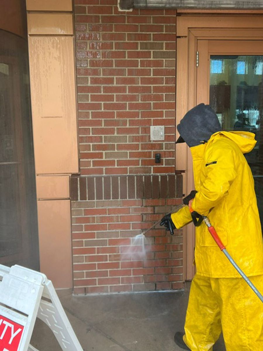 A man in a yellow PPE suit is spraying a brick wall