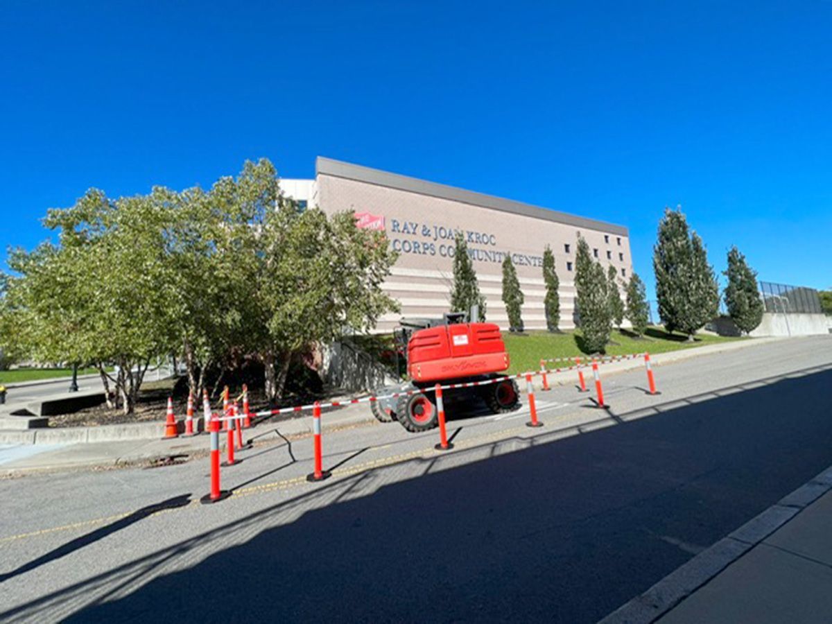 A red truck is parked on the side of the road in front of a large building