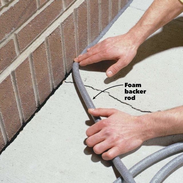 Hands installing foam backer rod between brick wall and concrete.