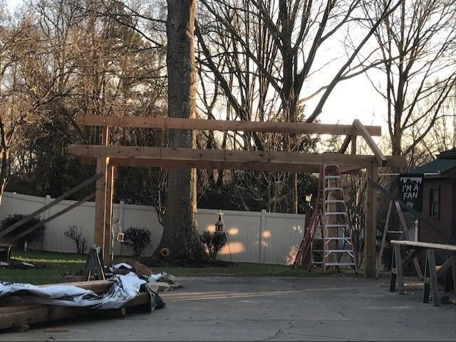 Backyard construction scene with a wooden pergola frame, ladder, and scattered materials at dusk