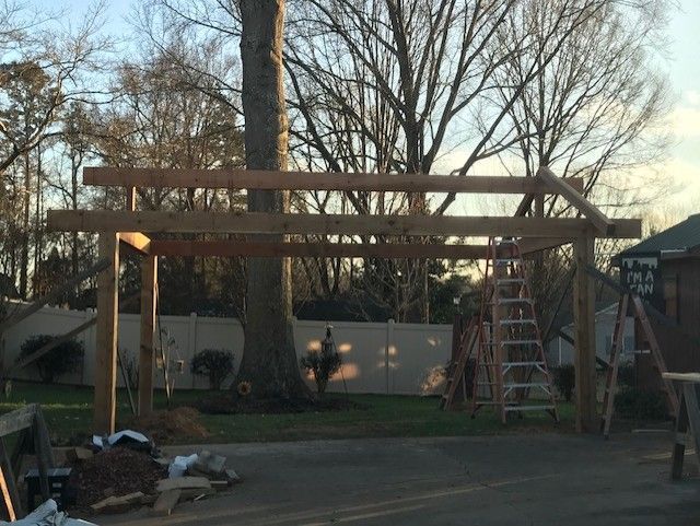 Wooden pergola frame under construction in a backyard at dusk, with ladder and tools nearby