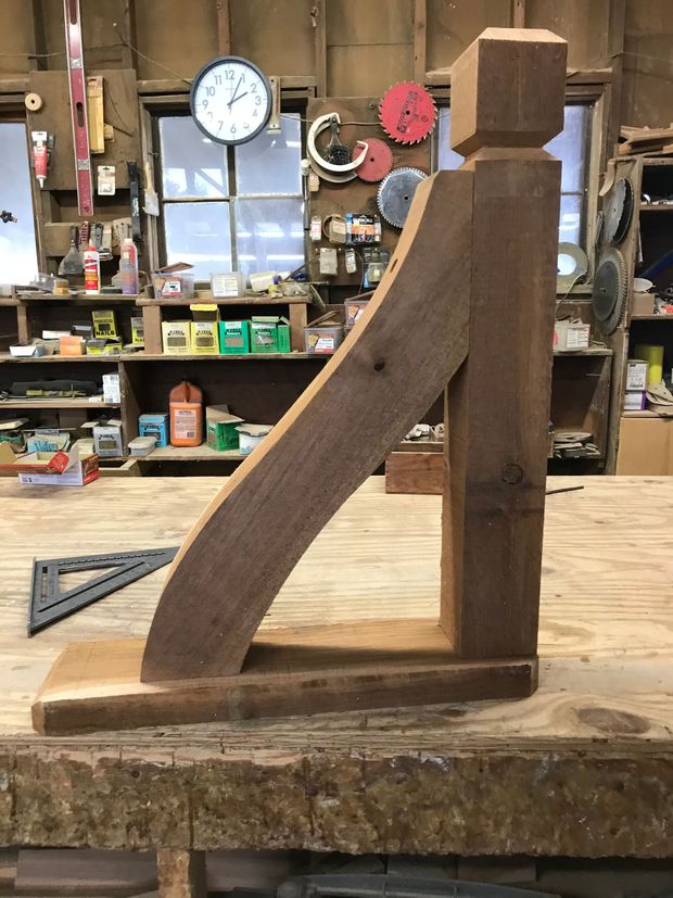 Wooden bracket prototype on a workbench in a cluttered workshop with tools and shelves in the background