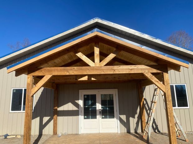 Front view of a tan building with a wooden porch and white double doors under a peaked roof.
