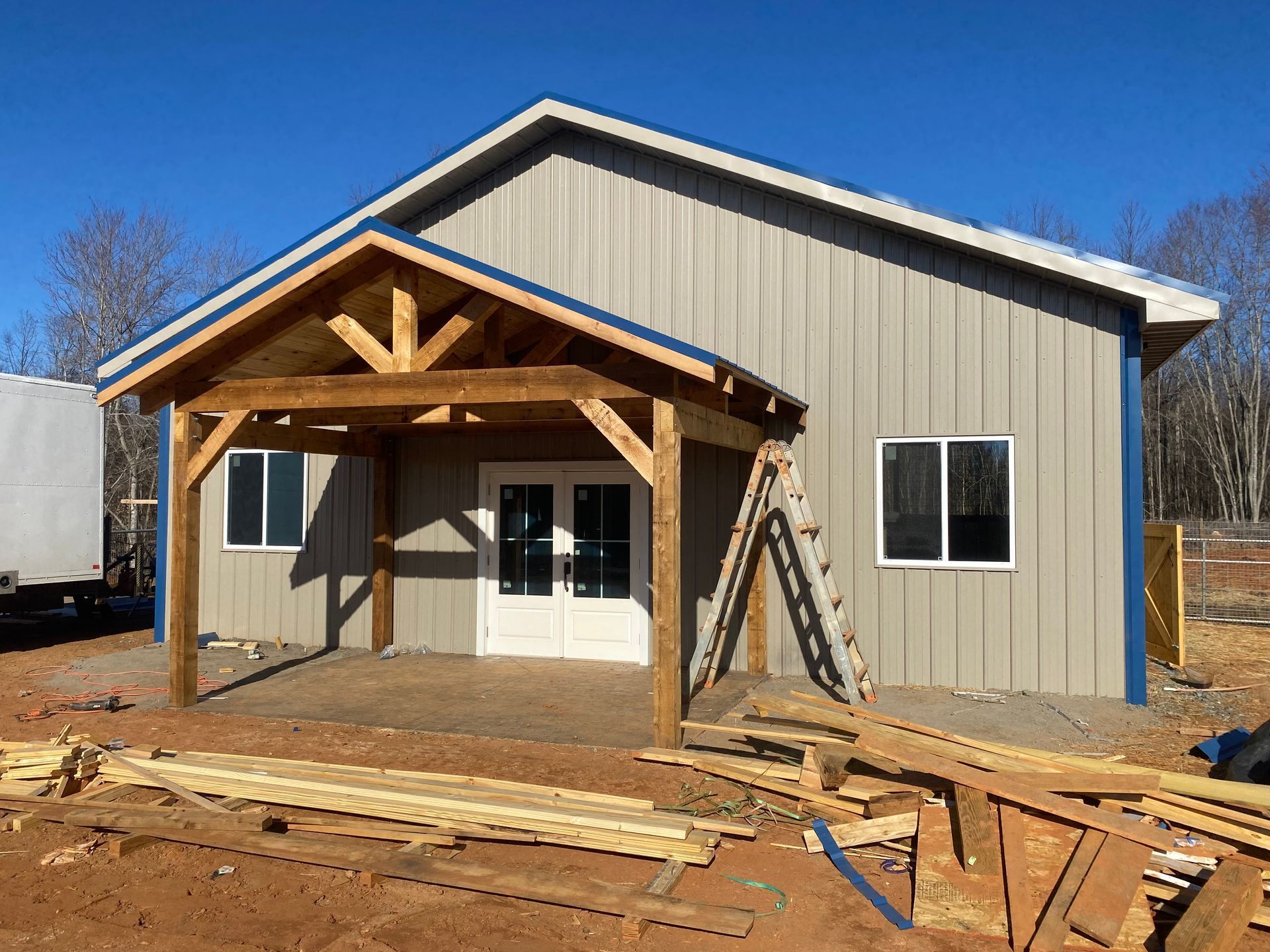 New metal building under construction with a covered front porch and lumber on the ground