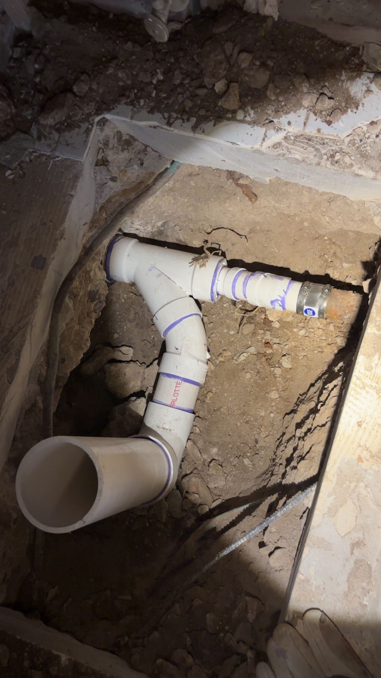 PVC drain pipes in a dirt trench. The pipes have multiple elbows and joints.