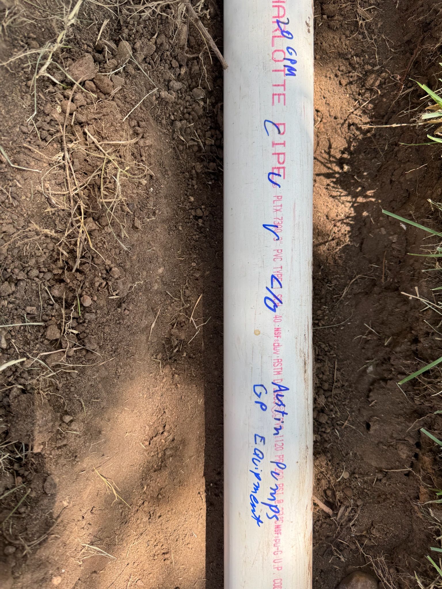 White PVC pipe laid in a trench of brown dirt with handwritten text.