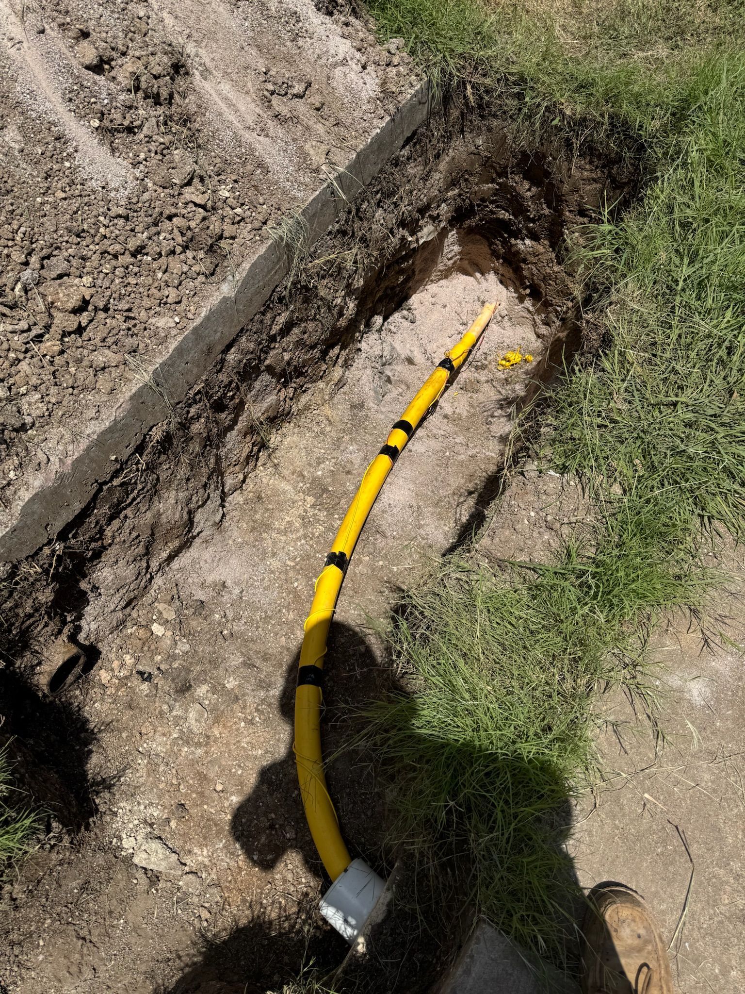 Yellow gas line in a trench in grass and dirt.